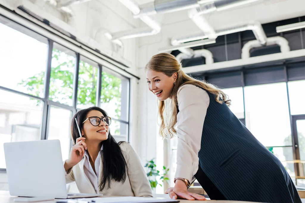 Two professional women in an office smiling at a laptop