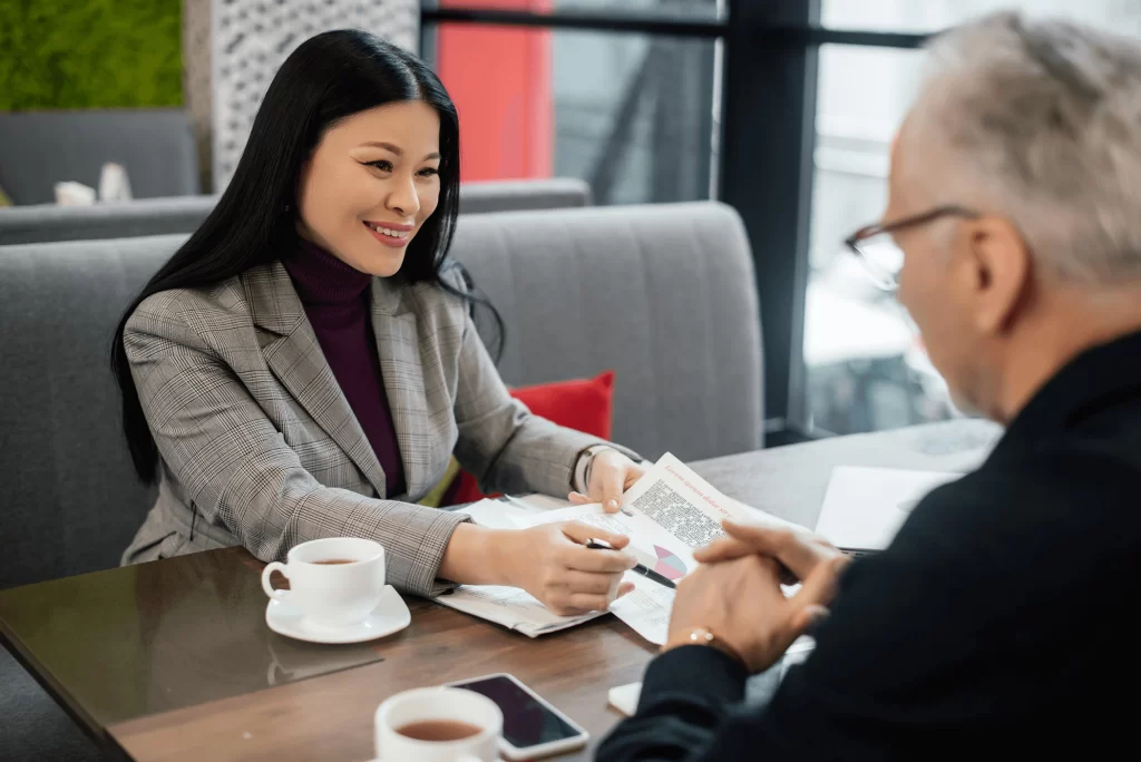 An Asian woman explaining printed graphics to a man in a coffee shop