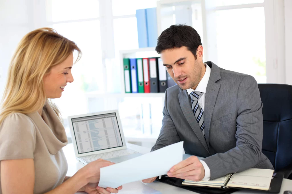 Two White professionals discussing a paper at an office desk