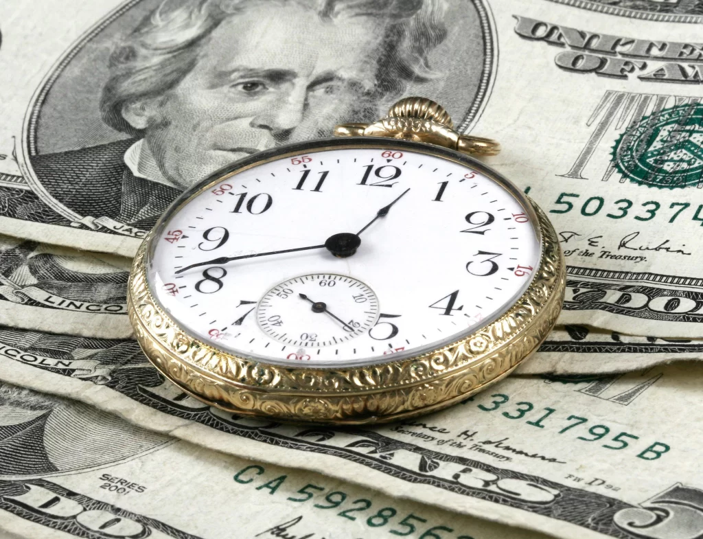 A gold pocket watch sitting on $5 and $20 bills
