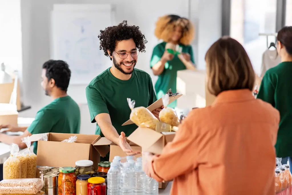 A man holding a clipboard accepts a box of donated food at a table covered in non-perishable food