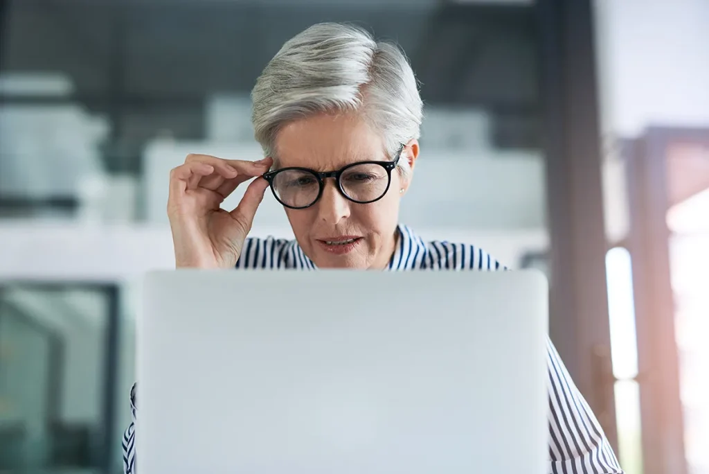 An older woman squinting at a laptop and adjusting her glasses