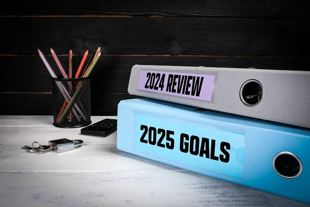 Two binders stacked on top of each other, the top on is labeled 2024 Review and the bottom is labeled 2025 Goals