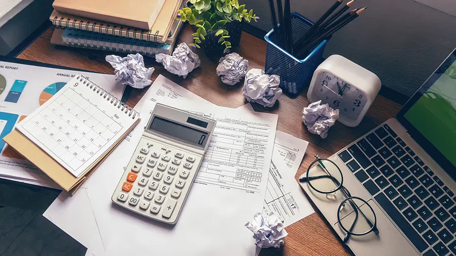 Laptop, and calculator for accountant or bookkeeper plan annual budget report and tax. Computer, Crumpled paper, and pencil placed on wooden table.