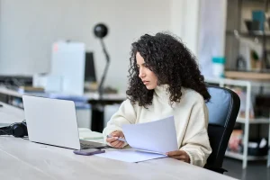 Young latin business woman accounting checking bills, working in office using laptop