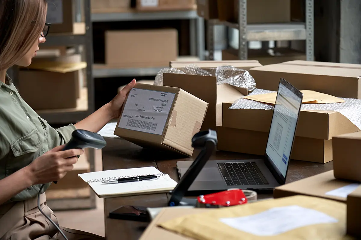Woman scanning labeled boxes with laptop in front of her.